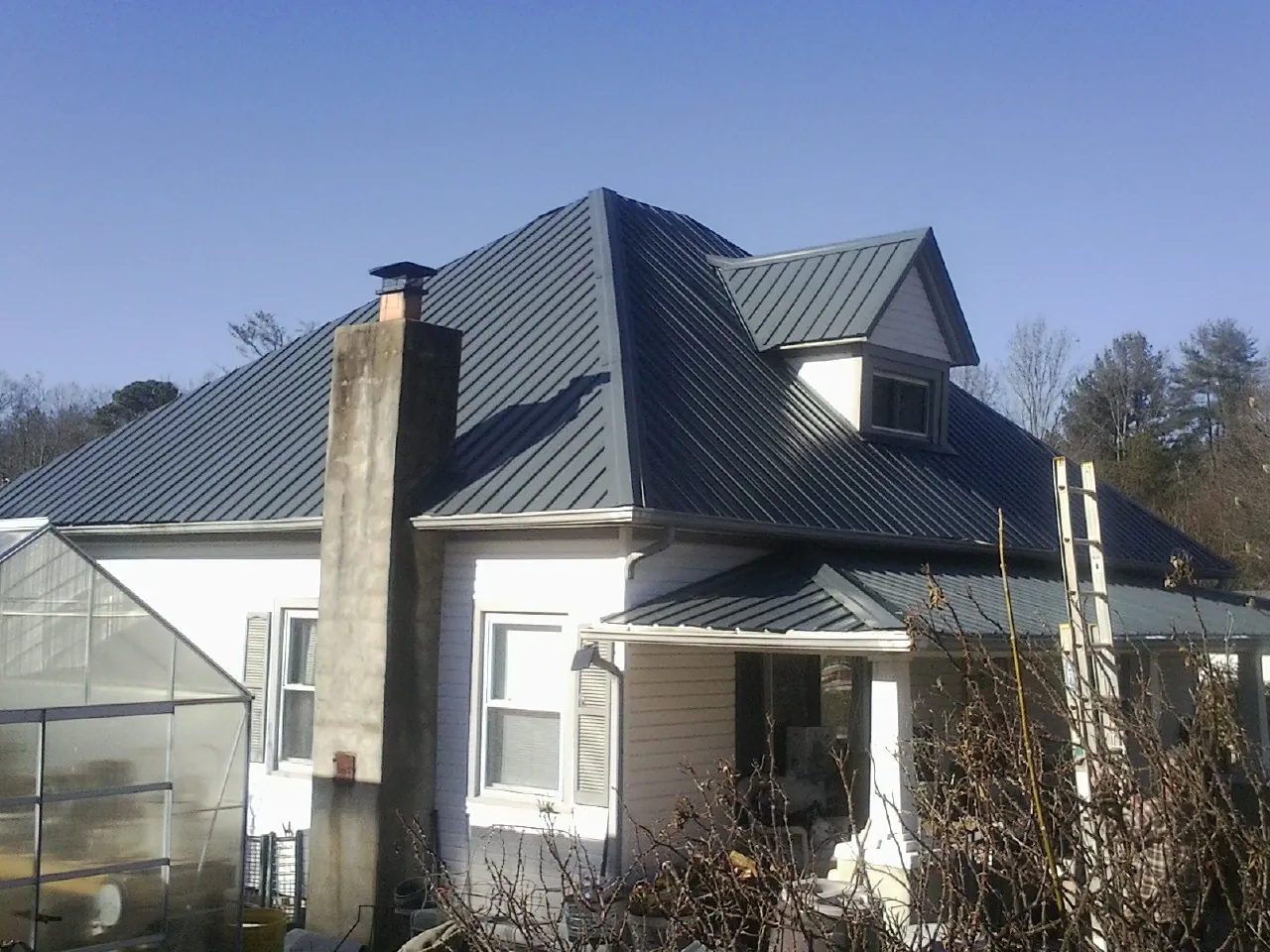 Dark blue standing seam metal roof on a white farmhouse with dormer — Slate & Tile Roof Repair by Roofing Brothers in Noble