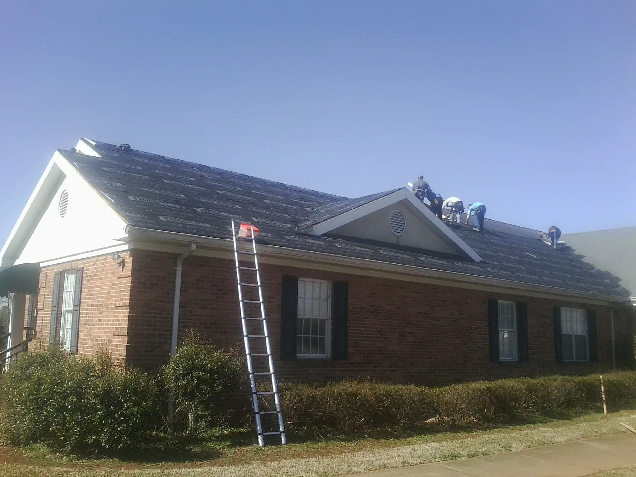 Crew tearing shingles off a brick ranch roof with a ladder set — Emergency Roof Repair work by our crew in Noble