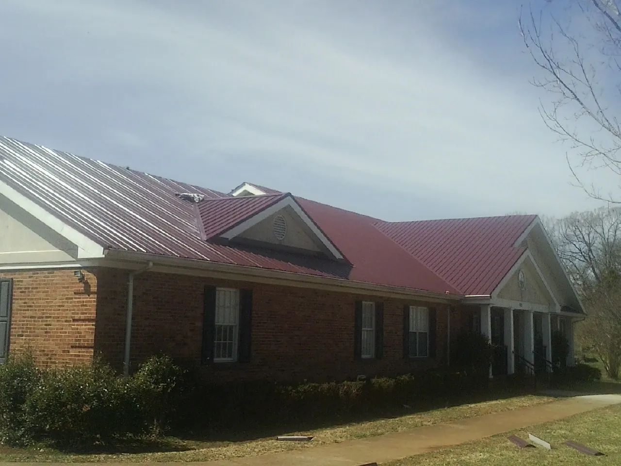 Red metal roof with gabled entries on a long brick building, from a Hail Damage Roof Repair job in Noble