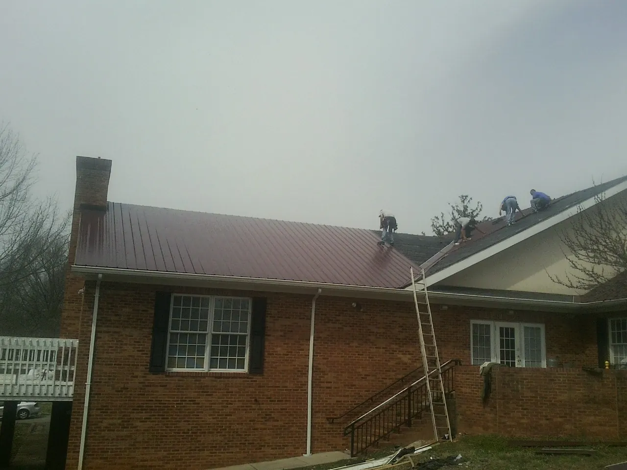 Crew setting red metal roofing panels on a brick home in Noble