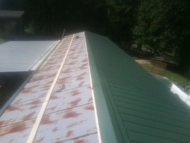 Old rusted panels beside newly installed green metal roofing — Wind Damage Roof Repair by Roofing Brothers in Noble