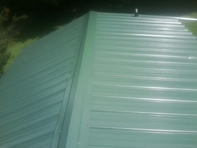 New green metal panels meeting at the ridge of a roof — Flat Roof Repair work by our crew in Noble