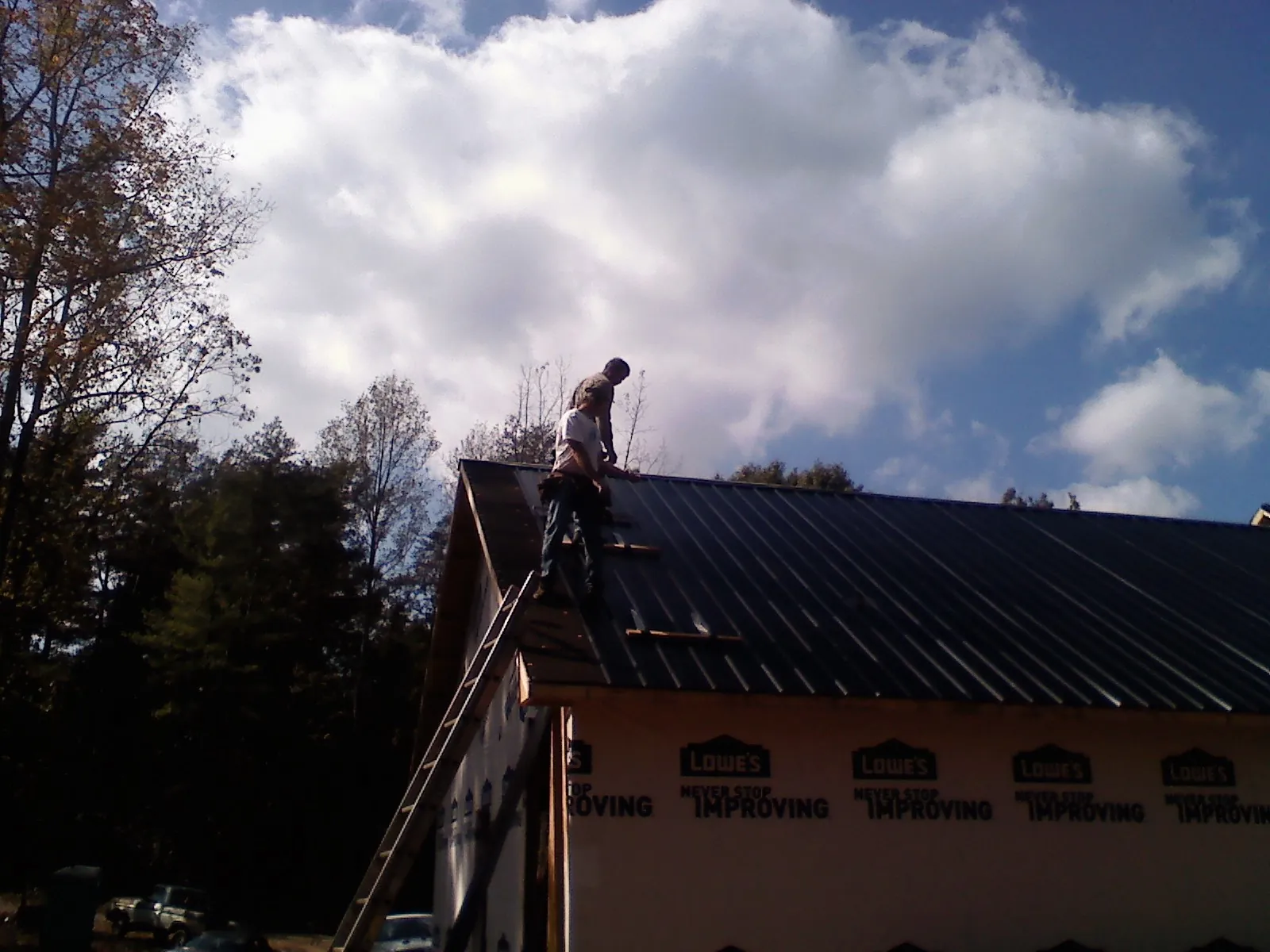 Roofer fastening dark metal panels high against a cloudy sky, from a Roof Inspection job in Noble