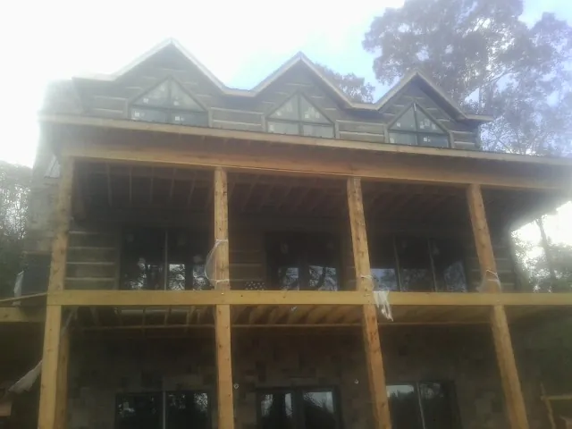 Dormers and porch framing on a large log home under construction — Roof Coating work by our crew in Noble