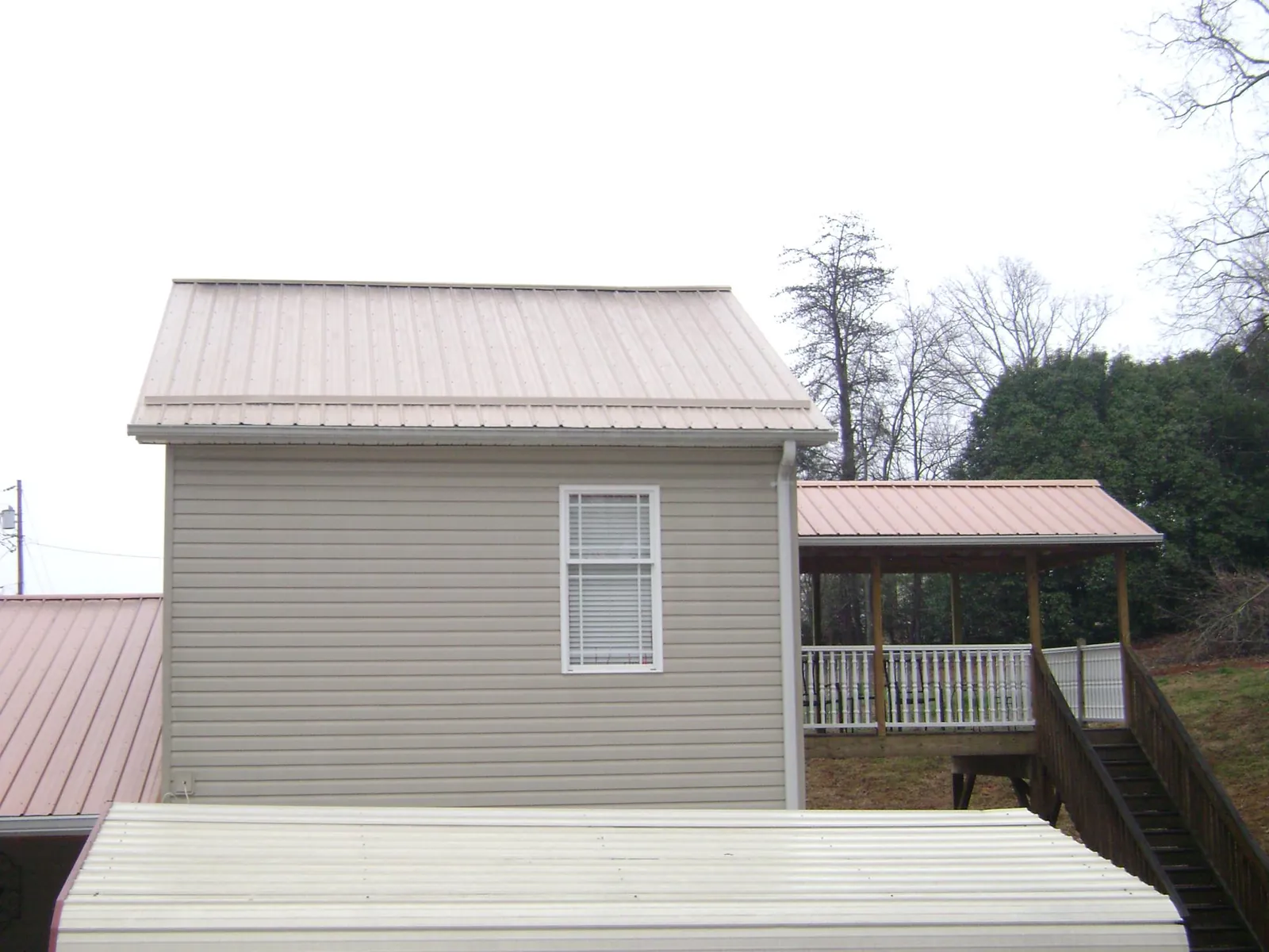 Tan metal roofs on a two story addition and attached porch, from a Roof Replacement job in Noble